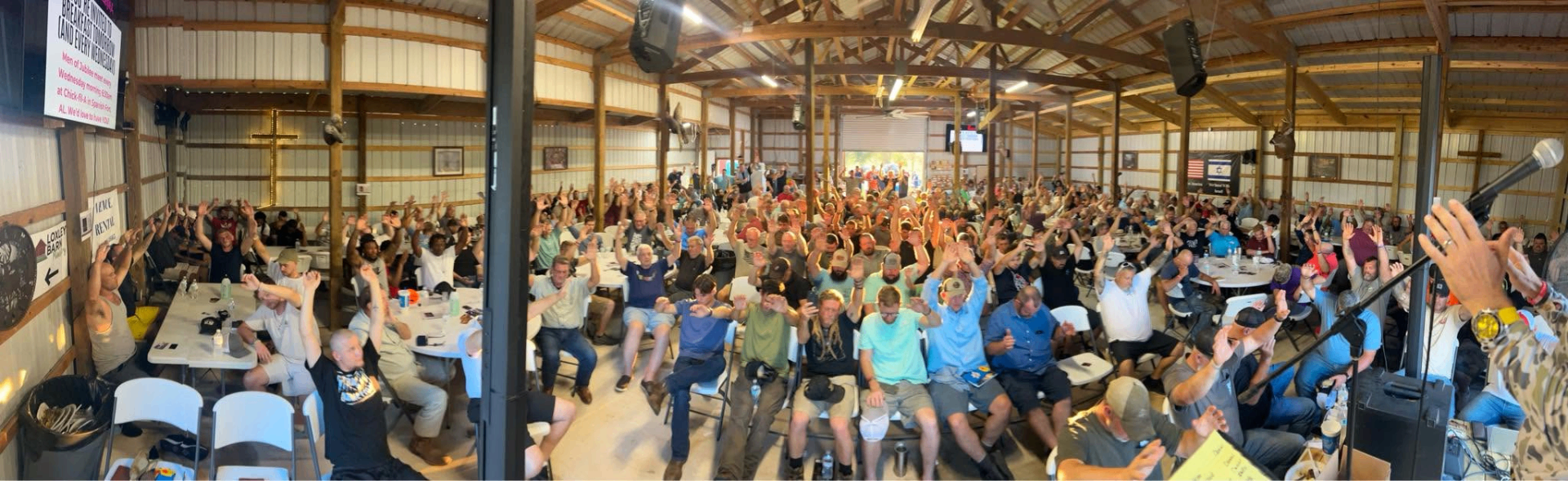 Panoramic view of hundreds of men inside The Loxley Barn with hands raised